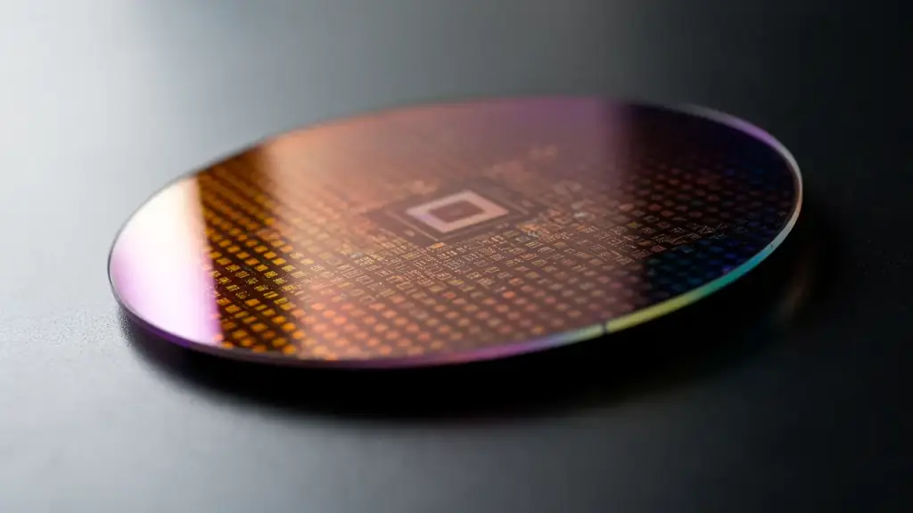 A silicon wafer catching a violet and copper sheen across its die grid